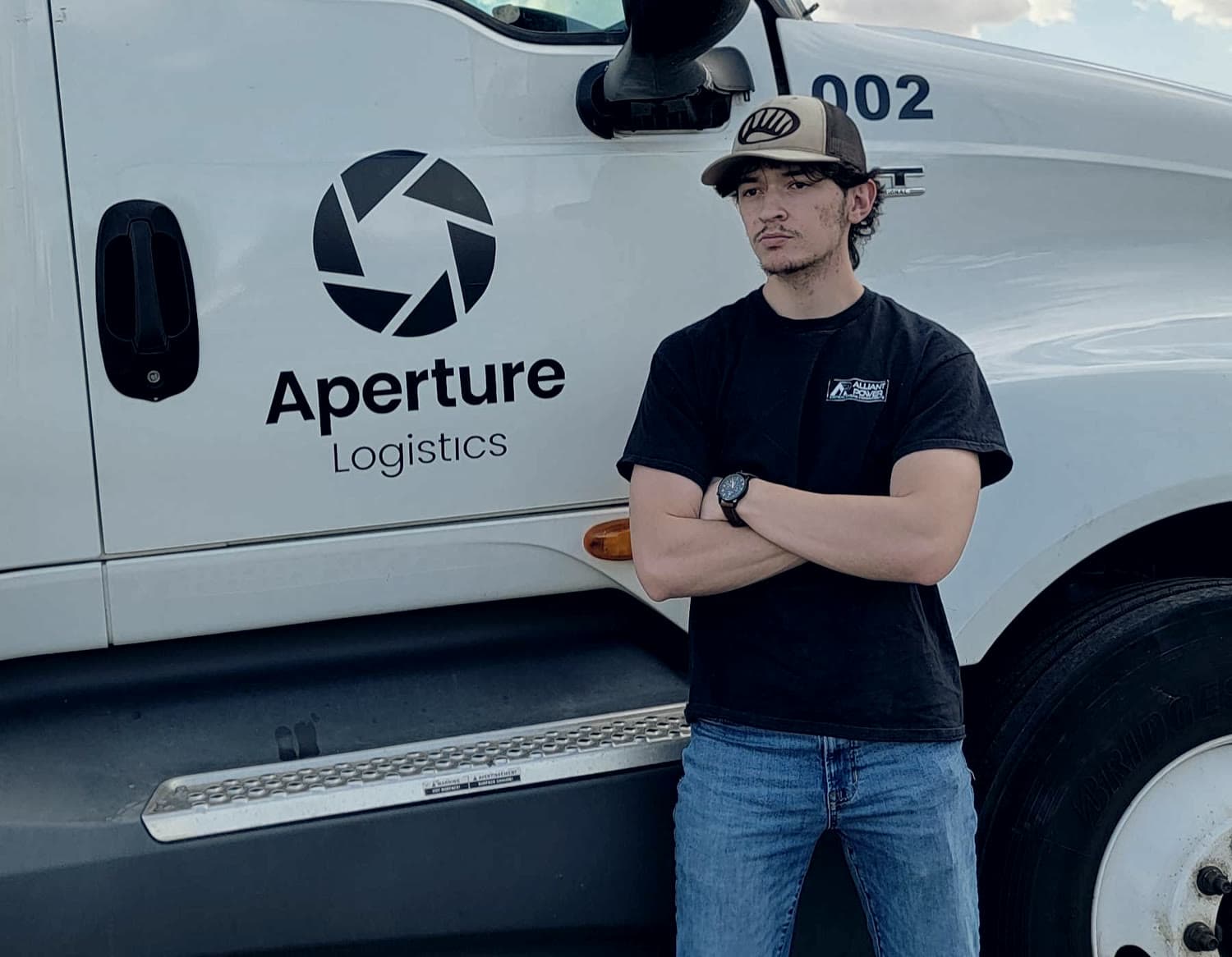 Truck 002, a white International LT625 carrying the Aperture Logistics mark on the cab door, with a member of the Aperture team standing beside it